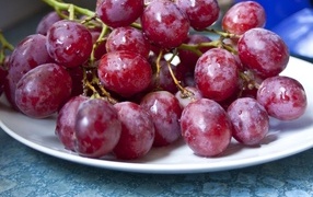 Спелый розовый виноград на белой тарелке