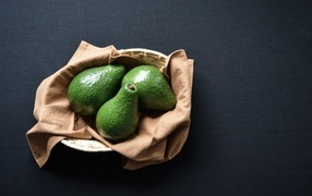 Три зеленых авокадо в корзинке на столе