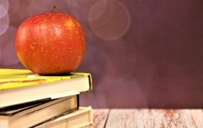 Мокрое яблоко на столе с книгами