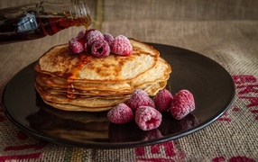 Thin pancakes on a black plate with raspberries and honey