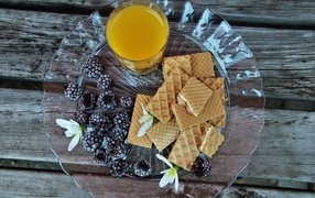 Вафли на тарелке с апельсиновым соком и ягодами замороженной ежевики