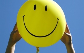 Желтый шарик с улыбкой в руках на голубом фоне