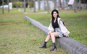 Девушка в пальто сидит на земле в парке