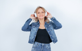 Девушка в джинсовом костюме с наушниками на голове на фоне стены