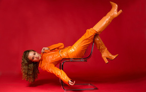 Девушка в кожаном костюме лежит на кресле на красном фоне