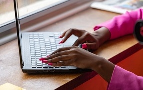 Девушка с розовым маникюром сидит за ноутбуком