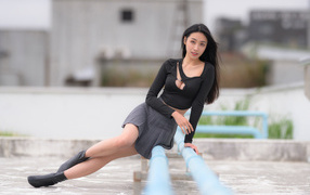 Девушка азиатка в черном наряде сидит на трубе