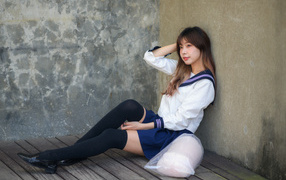 Азиатка в черных чулках сидит у стены