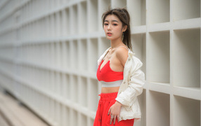 Азиатка в красном спортивном костюме стоит у стены