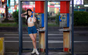 Азиатка в коротких шортах стоит у телефона-автомата