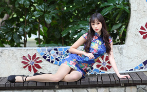 Красивая девушка азиатка в платье лежит на лавке