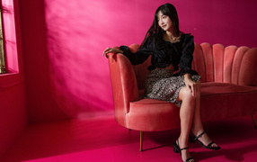 Красивая азиатка сидит на красном диване у окна