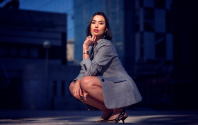 Красивая брюнетка в сером пиджаке сидит на корточках