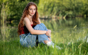 Красивая рыжеволосая девушка сидит в зеленой траве