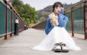 Милая азиатка с игрушечным медвежонком сидит на мосту