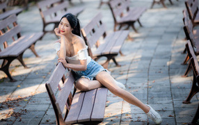 Милая девушка азиатка сидит на лавке в парке