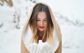 Милая девушка в капюшоне держит снег в ладонях