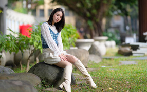 Милая девушка сидит на камне в парке