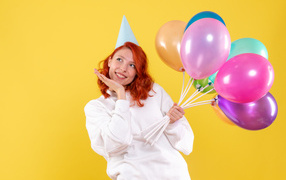 Милая рыжеволосая девушка с шариками на желтом фоне