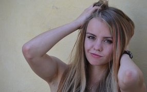 Девушка с руками в волосах у стены