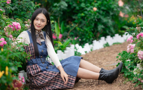 Настоящая молодая азиатка сидит на земле у клумбы