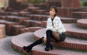 Грустная азиатка в шубе сидит на ступеньках
