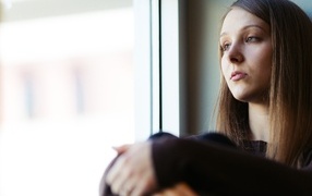 Грустная девушка сидит у окна
