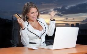 Довольная женщина с карточкой за столом с ноутбуком