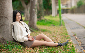 Улыбающаяся азиатка сидит под деревом в парке