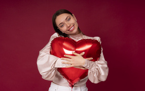 Улыбающаяся девушка обнимает шар в форме сердца