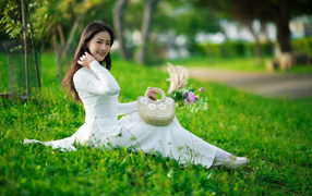 Нежная азиатка в белом наряде сидит на траве