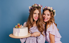 Две веселые молодые девушки с тортом на голубом фоне
