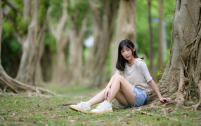 Молодая девушка азиатка сидит у дерева в парке