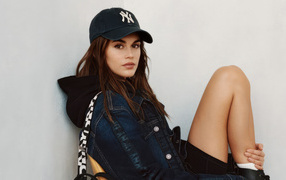 Красивая модель Кайя Гербер в кепке сидит у стены