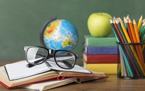 Книги, очки и карандаши с глобусом на столе у доски