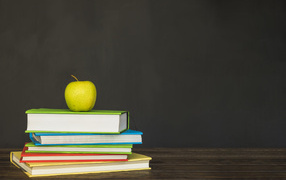 Разноцветные книги с зеленым яблоком на фоне доски