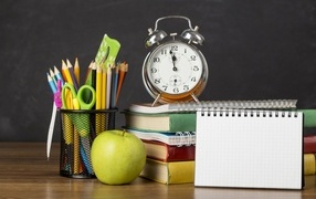 Канцелярские предметы на столе с будильником и книгами 