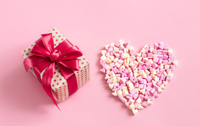 Подарок и сердце из конфет на розовом фоне