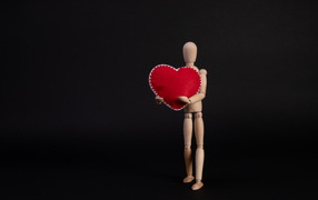 Марионетка держит красное сердце на черном фоне
