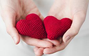 Два красных вязаных сердечка в руках девушки