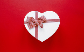 Белая коробка в форме сердца с бантом на красном фоне