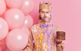 Мужчина принц с тортом и шариками на розовом фоне