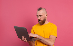 Удивленный мужчина с ноутбуком на розовом фоне