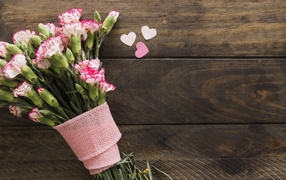 Розовые гвоздики с сердечками на коричневом деревянном фоне