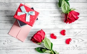 Две красные розы с подарком и сердечками на столе