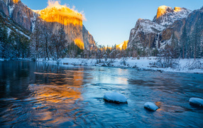 Холодная река с заснеженными берегами и горы в лучах солнца