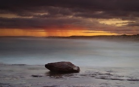Большой камень в воде на фоне грозового неба в море
