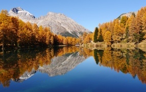 Осенний лес и гора отражаются  в воде озера