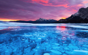 Красный закат солнца над горами у покрытого льдом озера