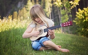 Девочка с маленькой гитарой сидит на траве
